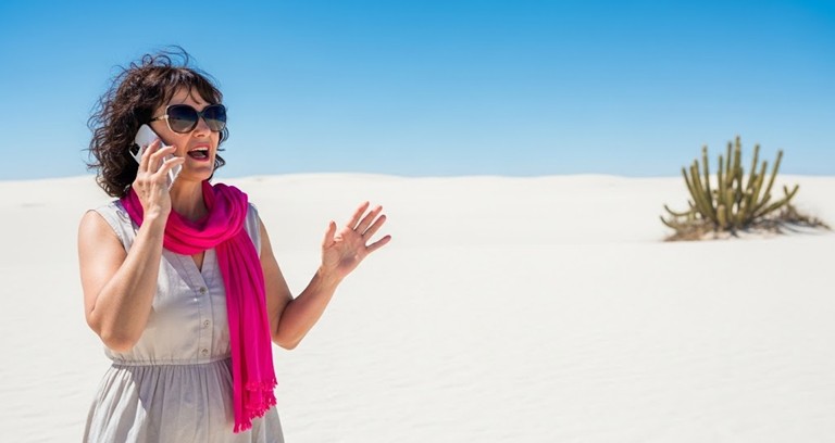 A woman standing in the middle of a desert talking on her phone