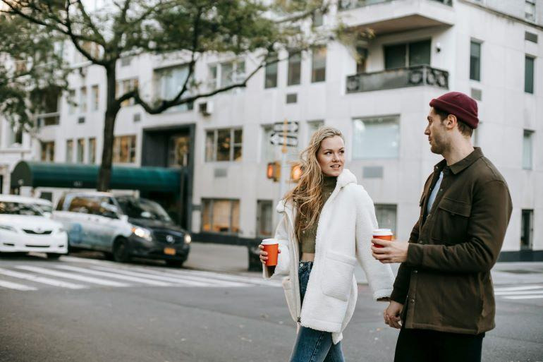 Two people walking with coffee cups along a city street, showing an easy and comfortable everyday routine.